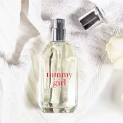 Tommy Girl Parfümflasche auf weißem Handtuch mit weißen Tulpen.