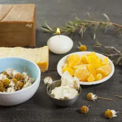 Bienenwachs, Kräuter und Seife für DIY-Kosmetik auf dunklem Holztisch.