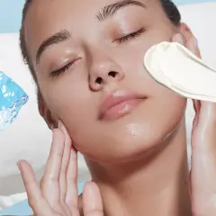 Frau mit geschlossenen Augen, Eiswürfel und Creme auf der Wange.