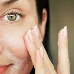 Nahaufnahme einer Frau, die sich eine Creme ins Gesicht aufträgt.