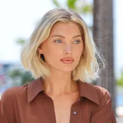 Blonde Frau mit mittellangem Haar und blauen Augen trägt braunes Hemd.