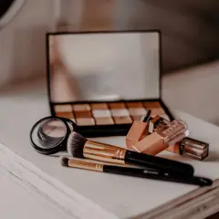 Make-up-Pinsel, Lidschattenpalette, Lippenstifte und Puder auf einer weißen Kommode.