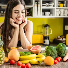 Lächelnde Frau mit frischem Obst und Gemüse auf einem Küchentisch.