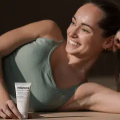 Lächelnde Frau liegt auf dem Boden und hält eine Handcreme.