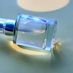 Ein klarer Glasflakon mit silbernem Sprühkopf liegt auf einer hellgrünen Oberfläche.