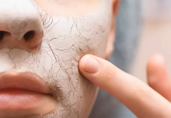 Nahaufnahme eines Gesichts mit trockener, rissiger Maske, auf die ein Finger tippt.
