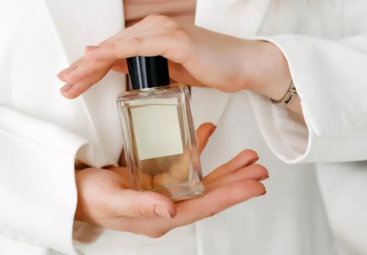Hände halten eine Glasflasche mit Parfum.