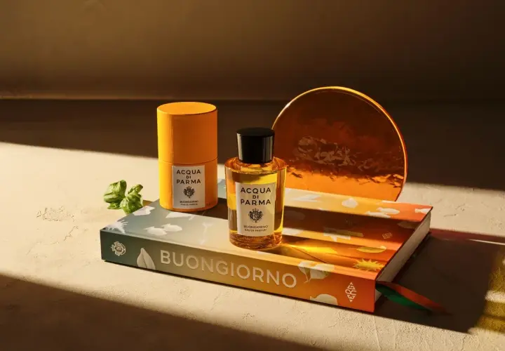 Acqua di Parma Flakon und Dose auf Buch mit "Buongiorno" Schriftzug, daneben ein grüner Zweig.