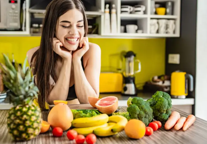 Lächelnde Frau mit frischem Obst und Gemüse auf einem Küchentisch.