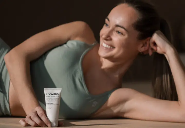 Lächelnde Frau liegt auf dem Boden und hält eine Handcreme.