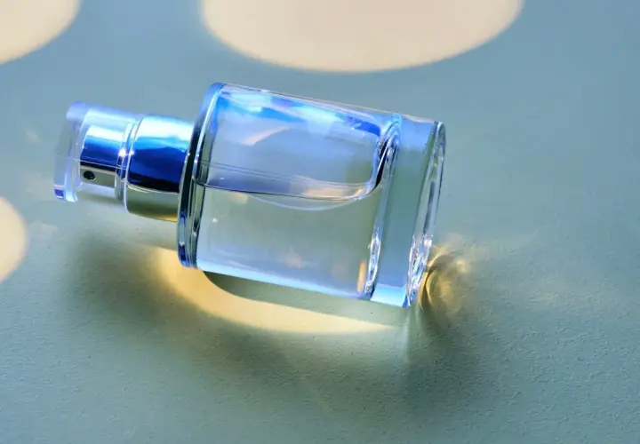 Ein klarer Glasflakon mit silbernem Sprühkopf liegt auf einer hellgrünen Oberfläche.