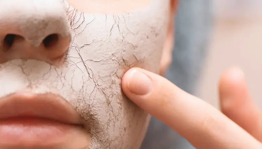 Nahaufnahme eines Gesichts mit trockener, rissiger Maske, auf die ein Finger tippt.