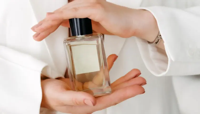 Hände halten eine Glasflasche mit Parfum.