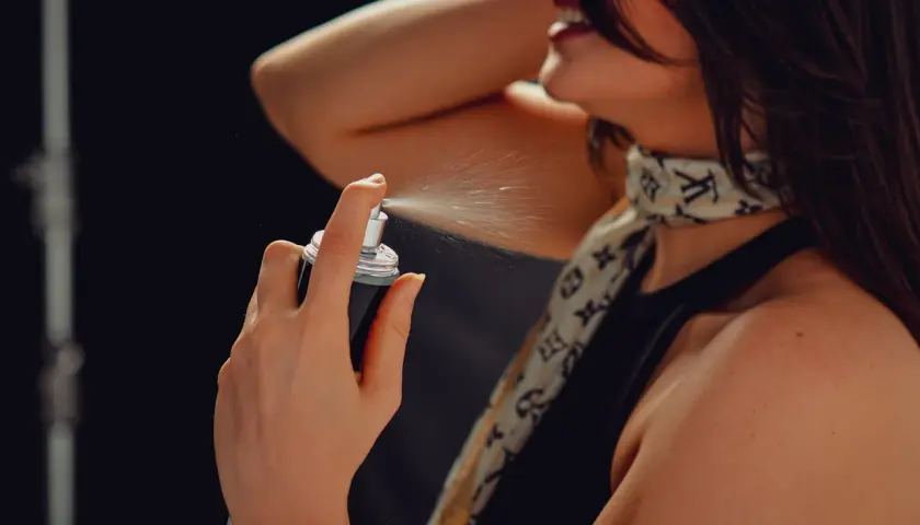 Frau sprüht sich Parfum auf den Hals, feiner Nebel verteilt sich.