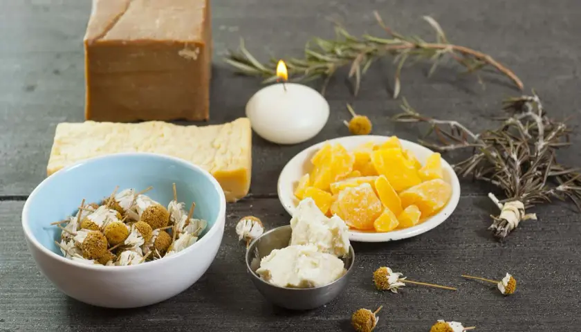 Bienenwachs, Kräuter und Seife für DIY-Kosmetik auf dunklem Holztisch.