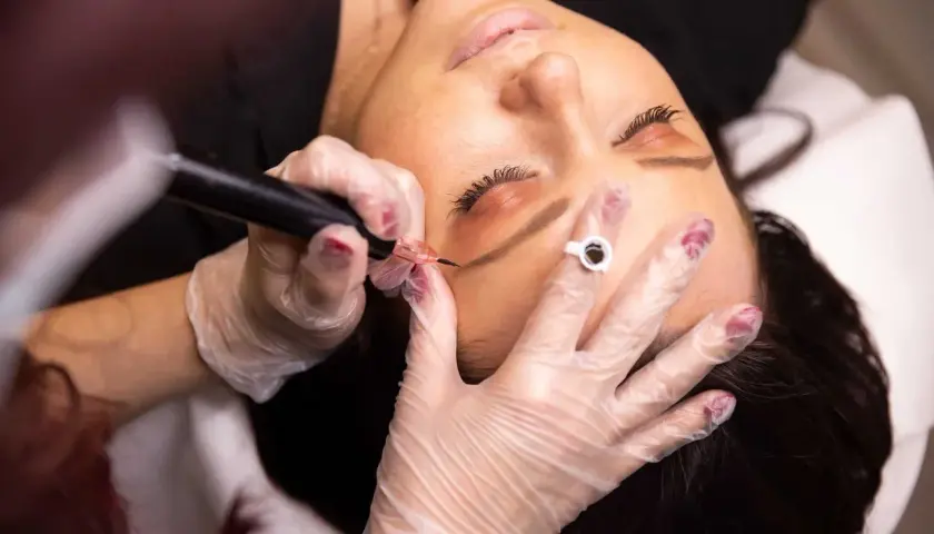 Nahaufnahme einer Frau, der mit einem Permanent-Make-up-Gerät die Augenbrauen pigmentiert werden.
