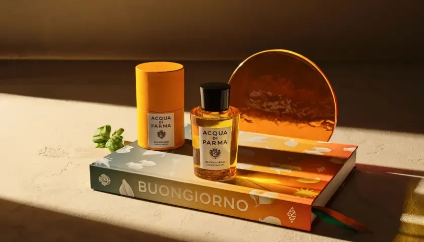 Acqua di Parma Flakon und Dose auf Buch mit "Buongiorno" Schriftzug, daneben ein grüner Zweig.