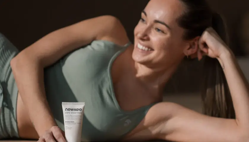 Lächelnde Frau liegt auf dem Boden und hält eine Handcreme.