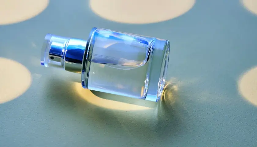 Ein klarer Glasflakon mit silbernem Sprühkopf liegt auf einer hellgrünen Oberfläche.