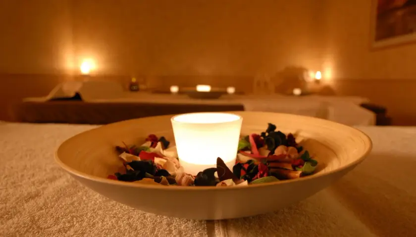 Eine leuchtende Kerze in einer Schale mit Potpourri auf einem Handtuch in einem Spa.