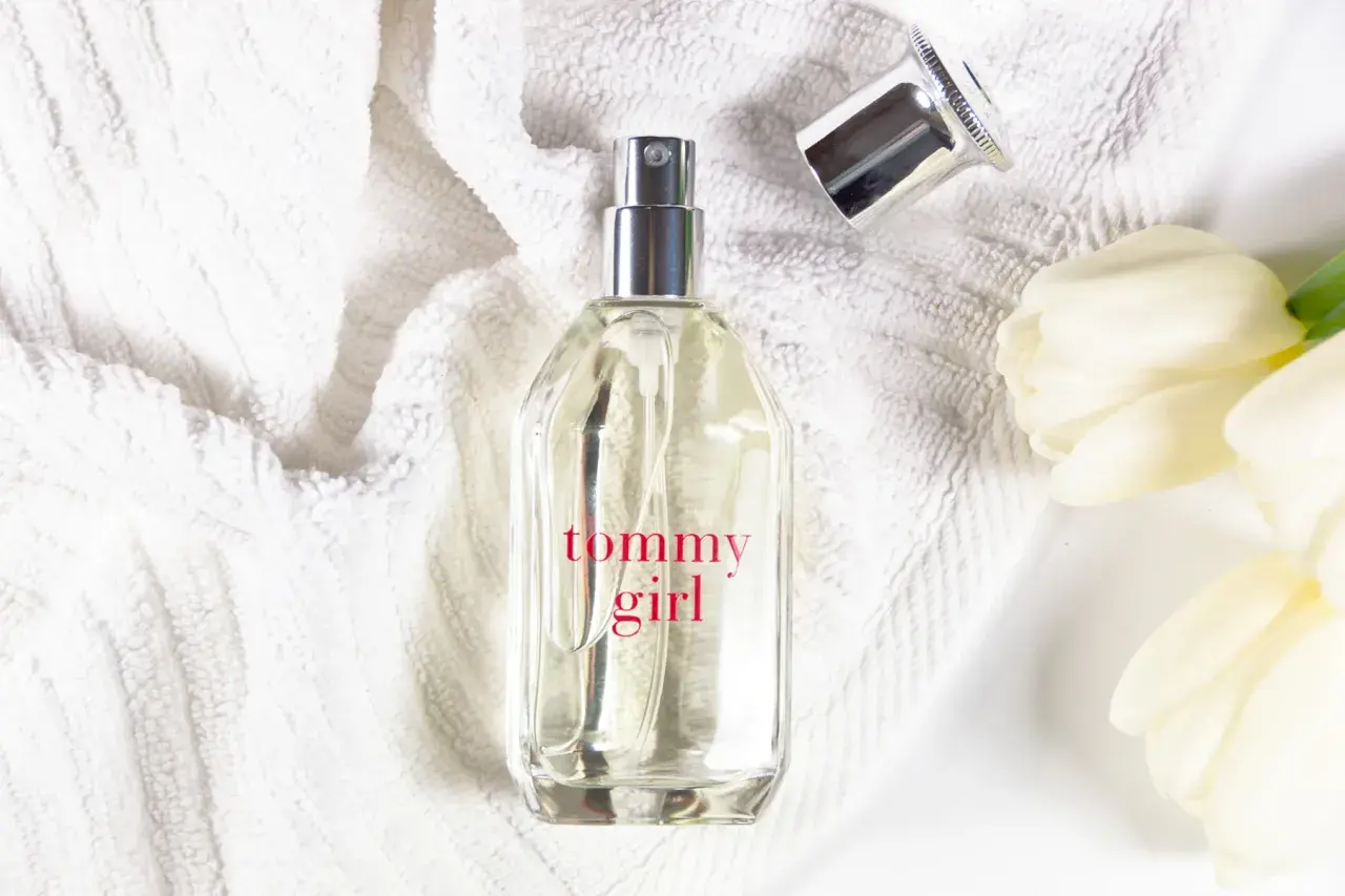 Tommy Girl Parfümflasche auf weißem Handtuch mit weißen Tulpen.