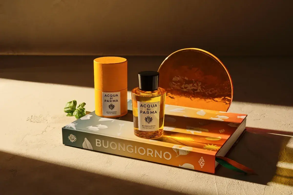 Acqua di Parma Flakon und Dose auf Buch mit "Buongiorno" Schriftzug, daneben ein grüner Zweig.