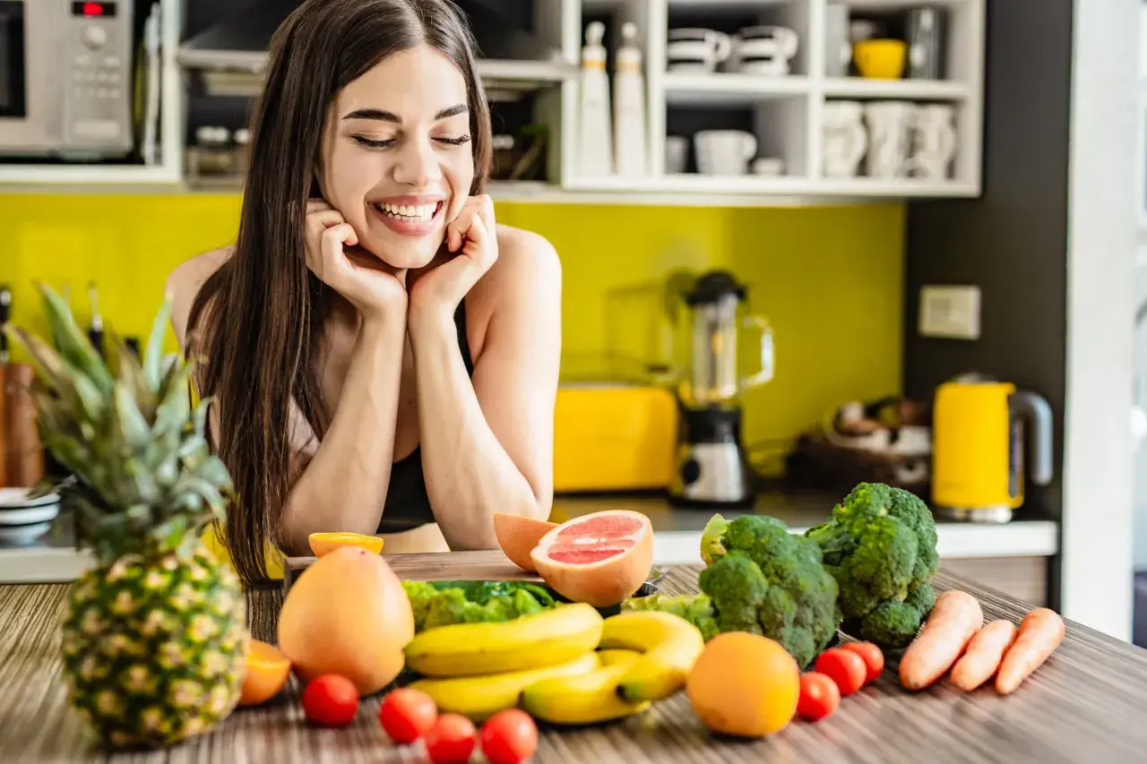 Lächelnde Frau mit frischem Obst und Gemüse auf einem Küchentisch.