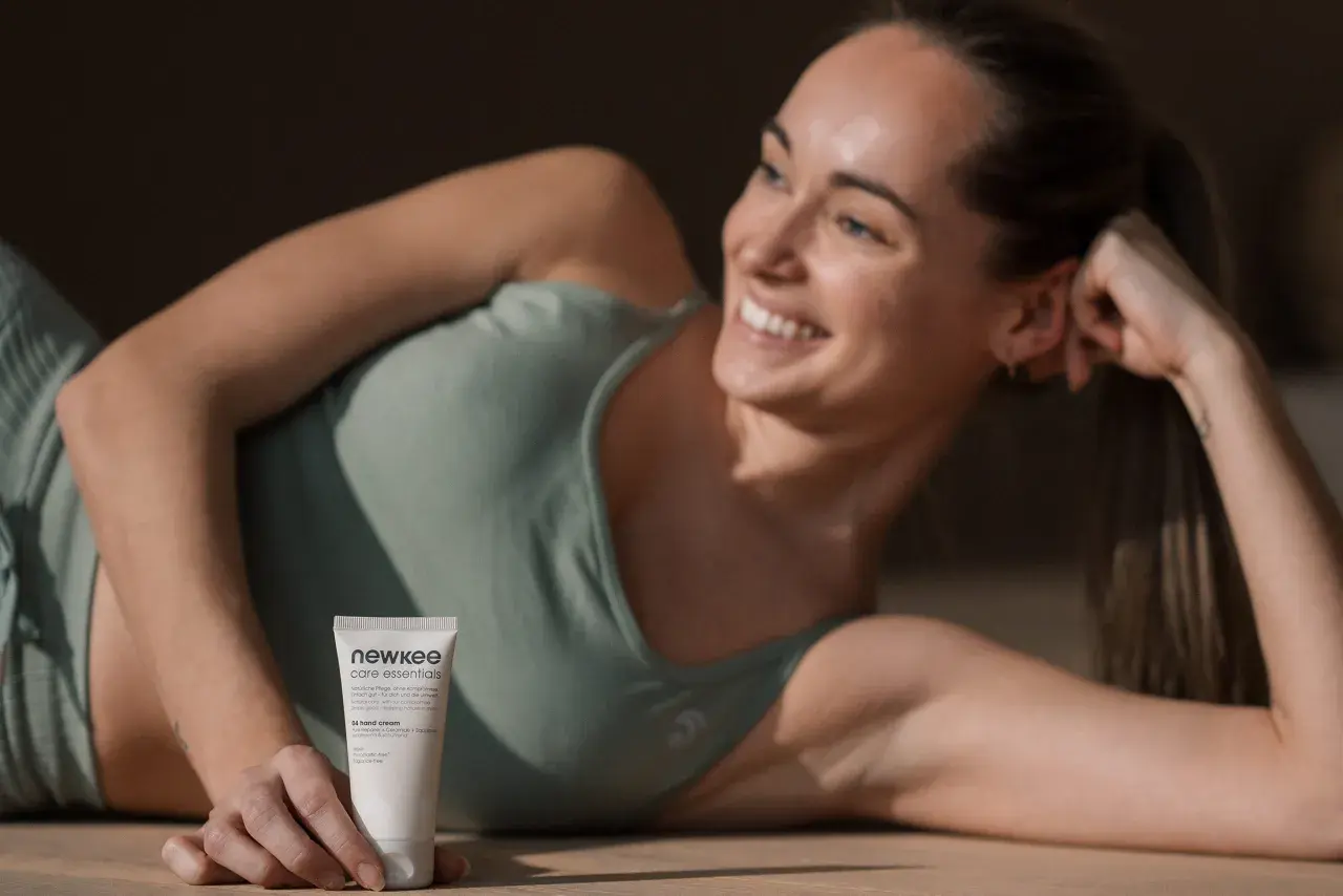 Lächelnde Frau liegt auf dem Boden und hält eine Handcreme.