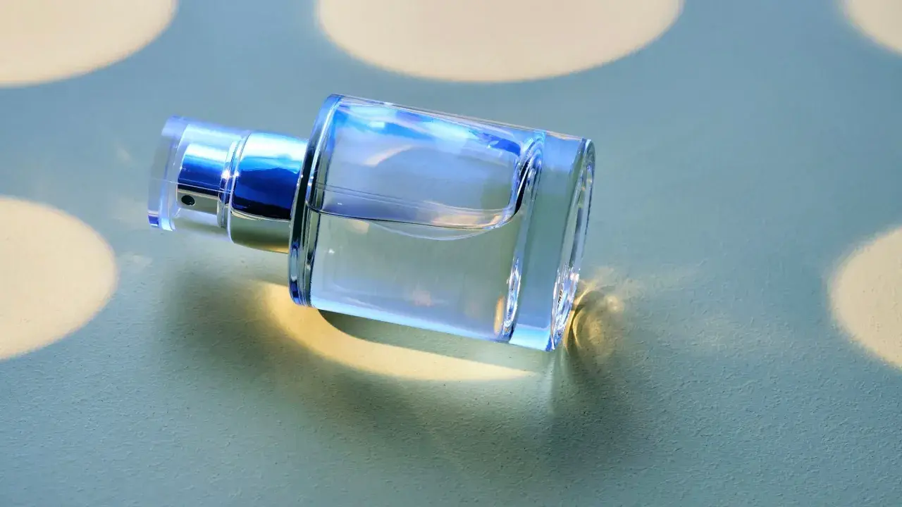 Ein klarer Glasflakon mit silbernem Sprühkopf liegt auf einer hellgrünen Oberfläche.