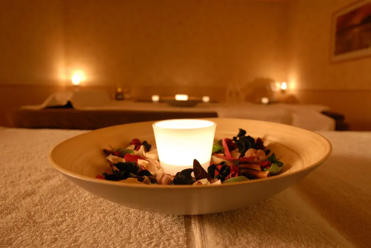 Eine leuchtende Kerze in einer Schale mit Potpourri auf einem Handtuch in einem Spa.